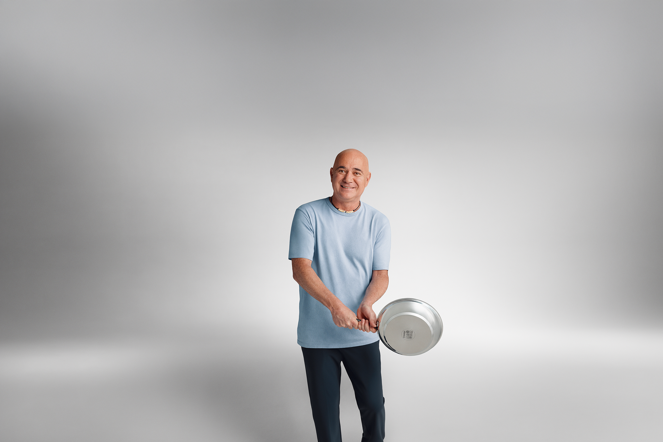 Andre Agassi sinisessä T-paidassa pitelee paistinpannua käsissään.