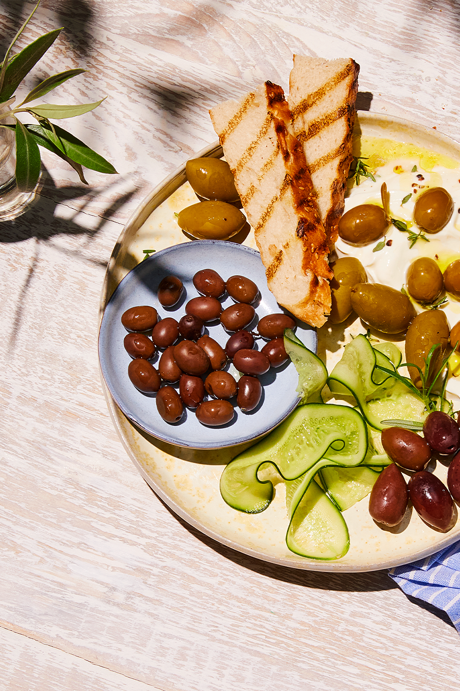 Lajitelma oliiveja, grillattua leipää ja kurkkua tarjoilulautasella.