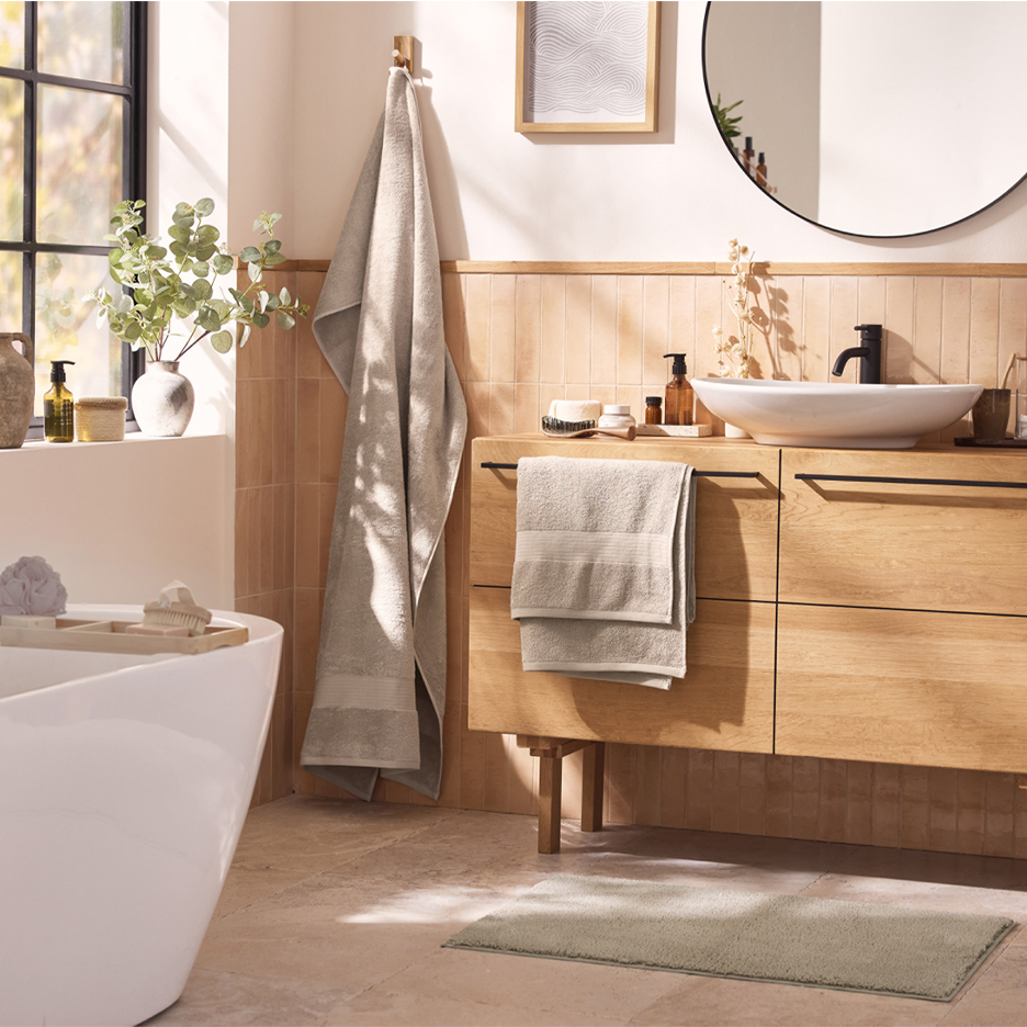 Kylpyhuone, jossa on puinen allaskaappi, valkoinen amme ja vaaleita pyyhkeitä.