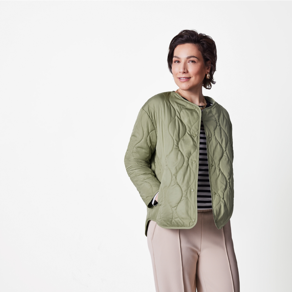 Nainen vihreässä tikkitakissa, raidallisessa paidassa ja beigenvärisissä housuissa.