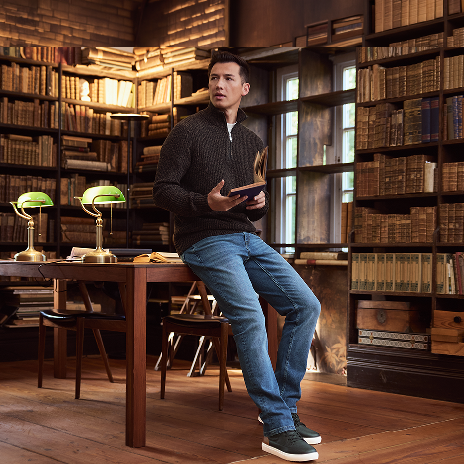 Mies neulepuserossa ja farkuissa lukee kirjaa kirjastossa.