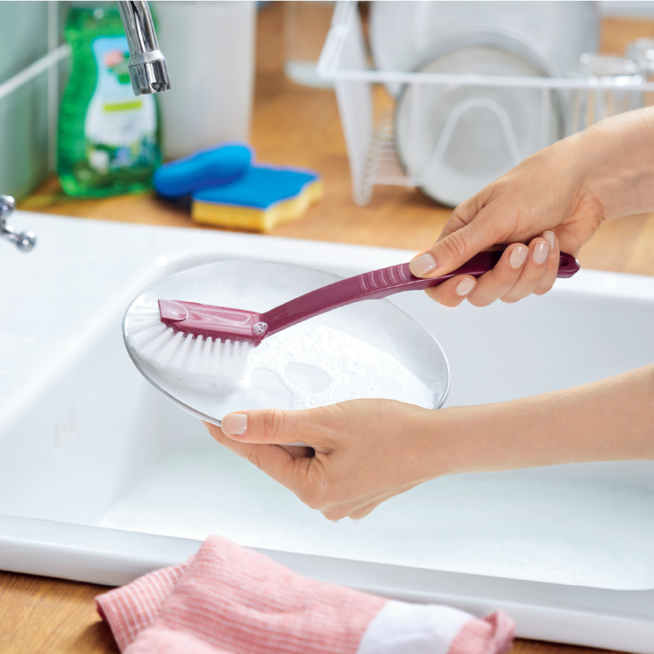 Kädet pesevät lautasta tiskiharjalla tiskialtaassa.